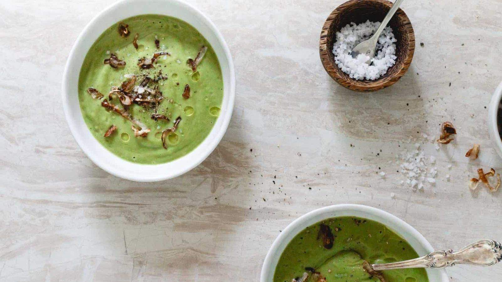 Top view of two bowls of creamy vegan broccoli soup with crispy shallots.