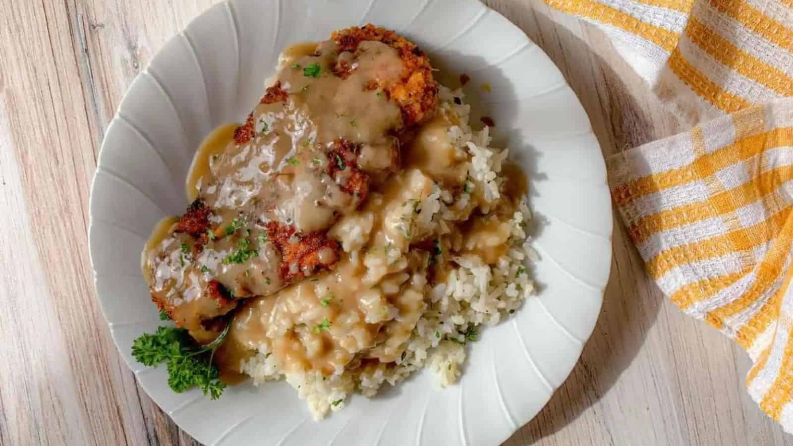 A dinner plate filled with pan fried chicken, rice, and gravy.