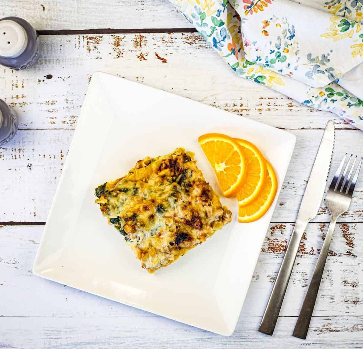 A white plate with a slice of Croissant breakfast casserole and orange next to it.