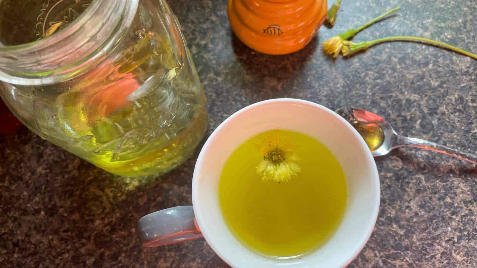 A cup of dandelion tea on a counter with a mason jar of tea and a spoon with honey.