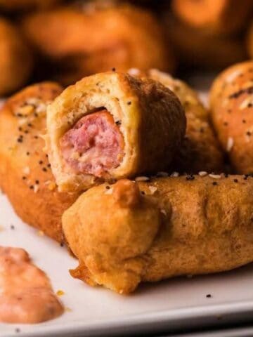 Everything bagel beer dogs with dipping sauce on a stack of small plates.