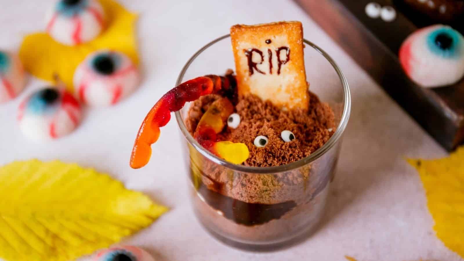 A glass of Halloween graveyard chocolate pudding with tombstone cookie on top that reads RIP.