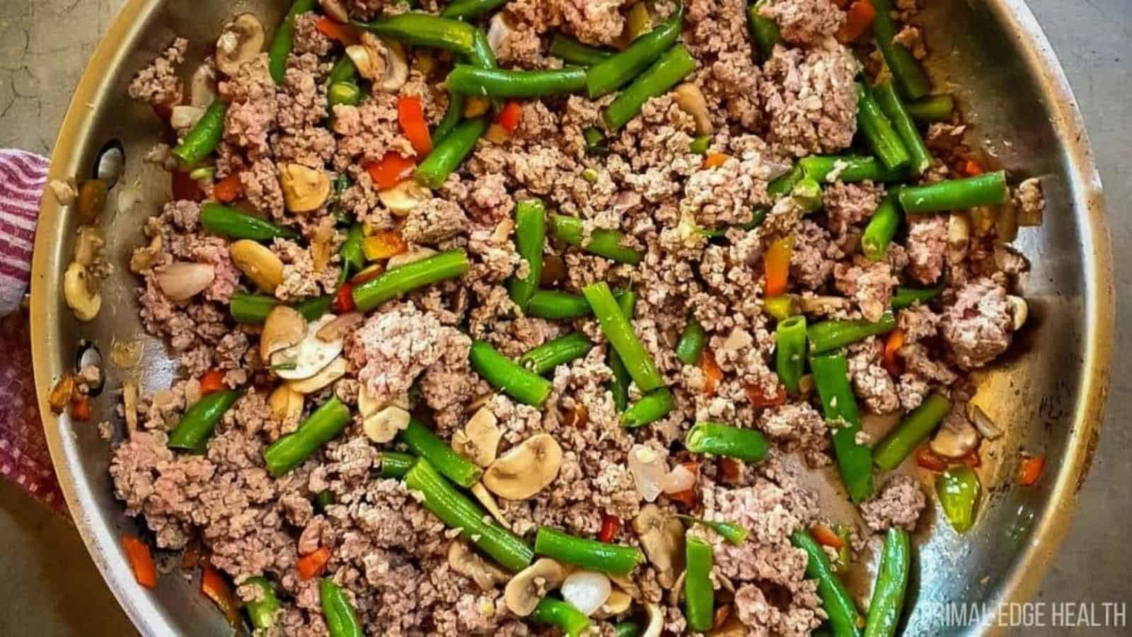 A picture of ground beef and green bean stir-fry in stainless steel skillet.