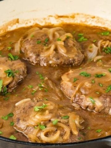 Close-up image of hamburger steak and gravy with a spoon in a pan.