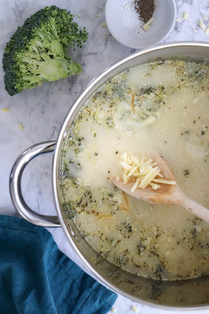 Close-up image of shredded cheddar in a wooden laddle being added to the soup.