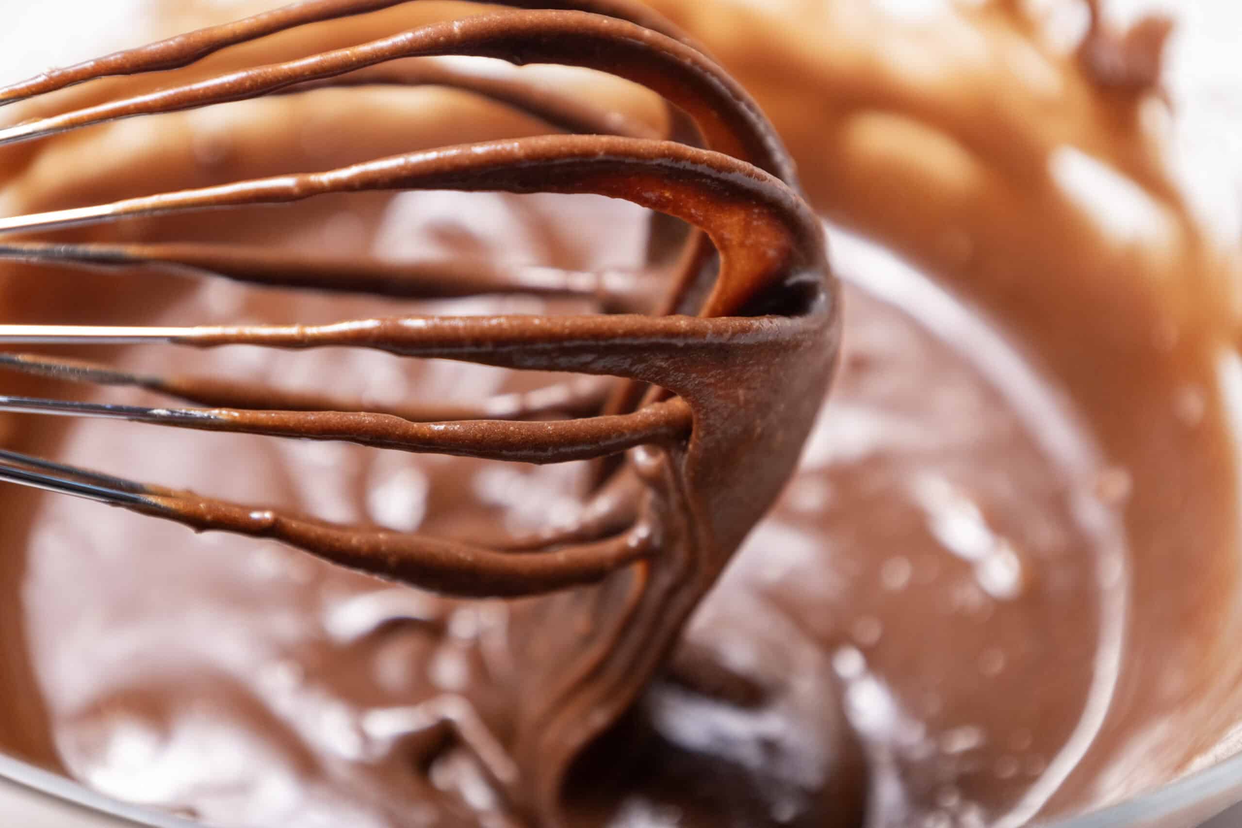 Close-up image of a whisk held above the mixture with batter sticking to the whisk.