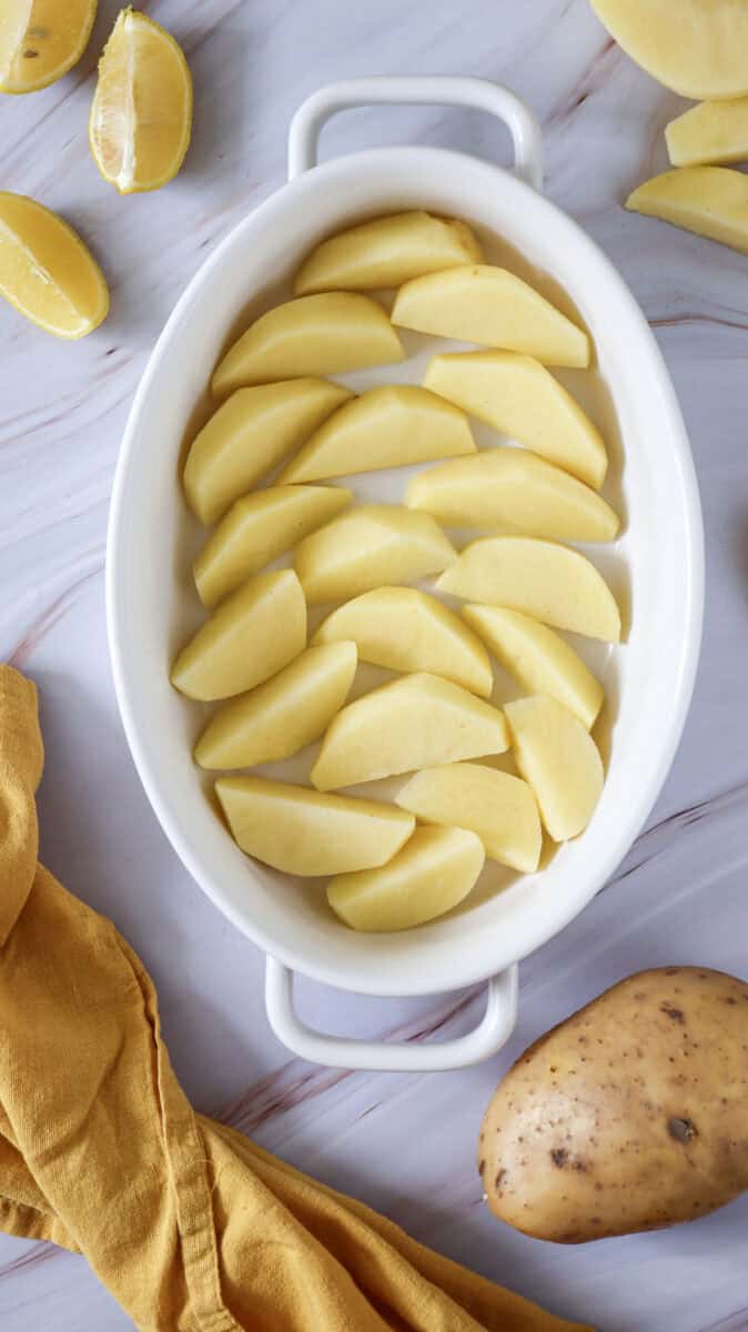 "Overhead image of sliced potatoes in a dish, with whole and sliced potatoes and lemon slices lying on the table.