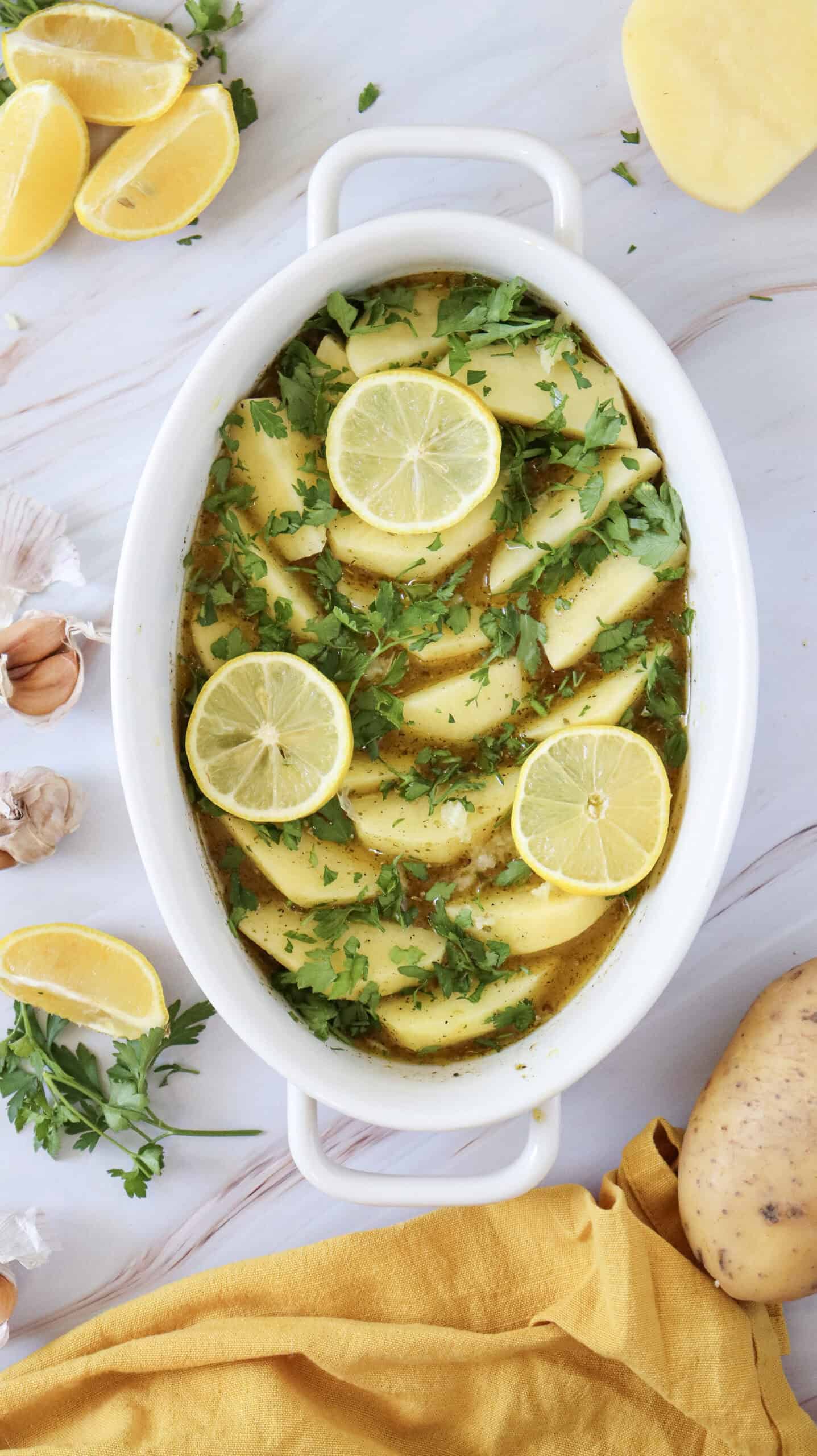 Overhead image of potato wedges in a dish with a liquid mixture and chopped parsley on top.