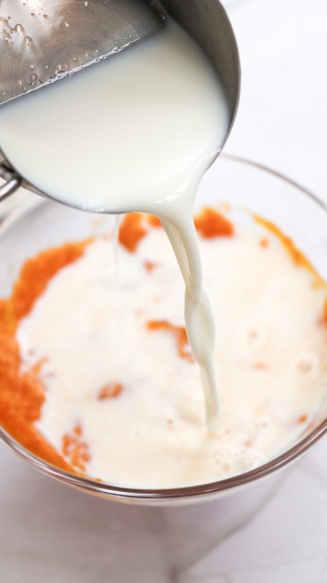 Close-up image of milk being poured into a bowl with pumpkin puree.