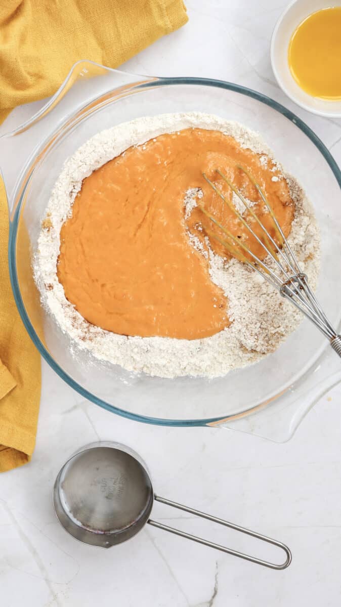 Overhead image of wet ingredients on top of dry ingredients in a bowl, with a whisk.