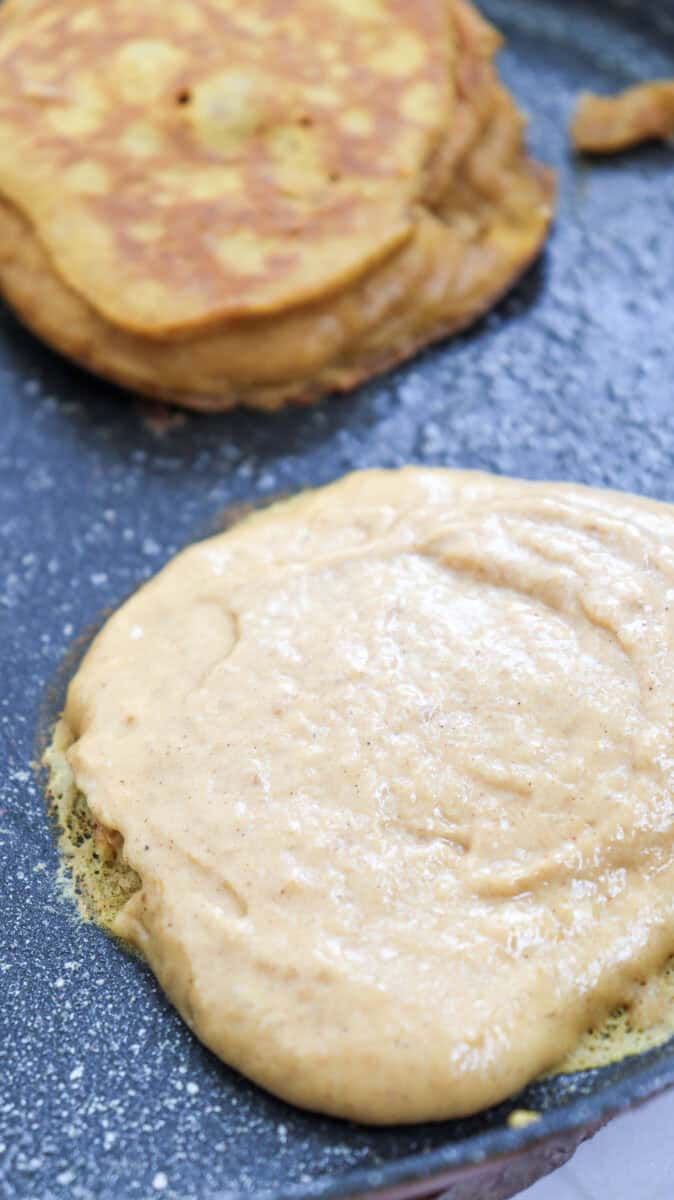 Close-up image of two pancakes cooking in a non-stick skillet.