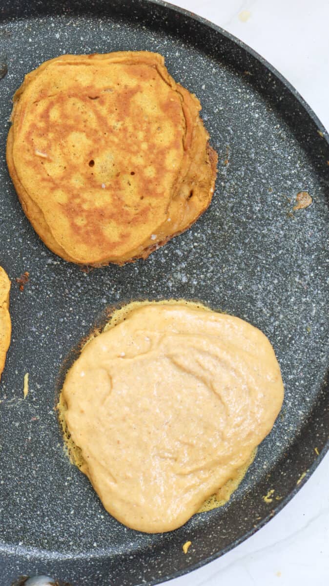 Overhead image of two pancakes cooking in a non-stick skillet.