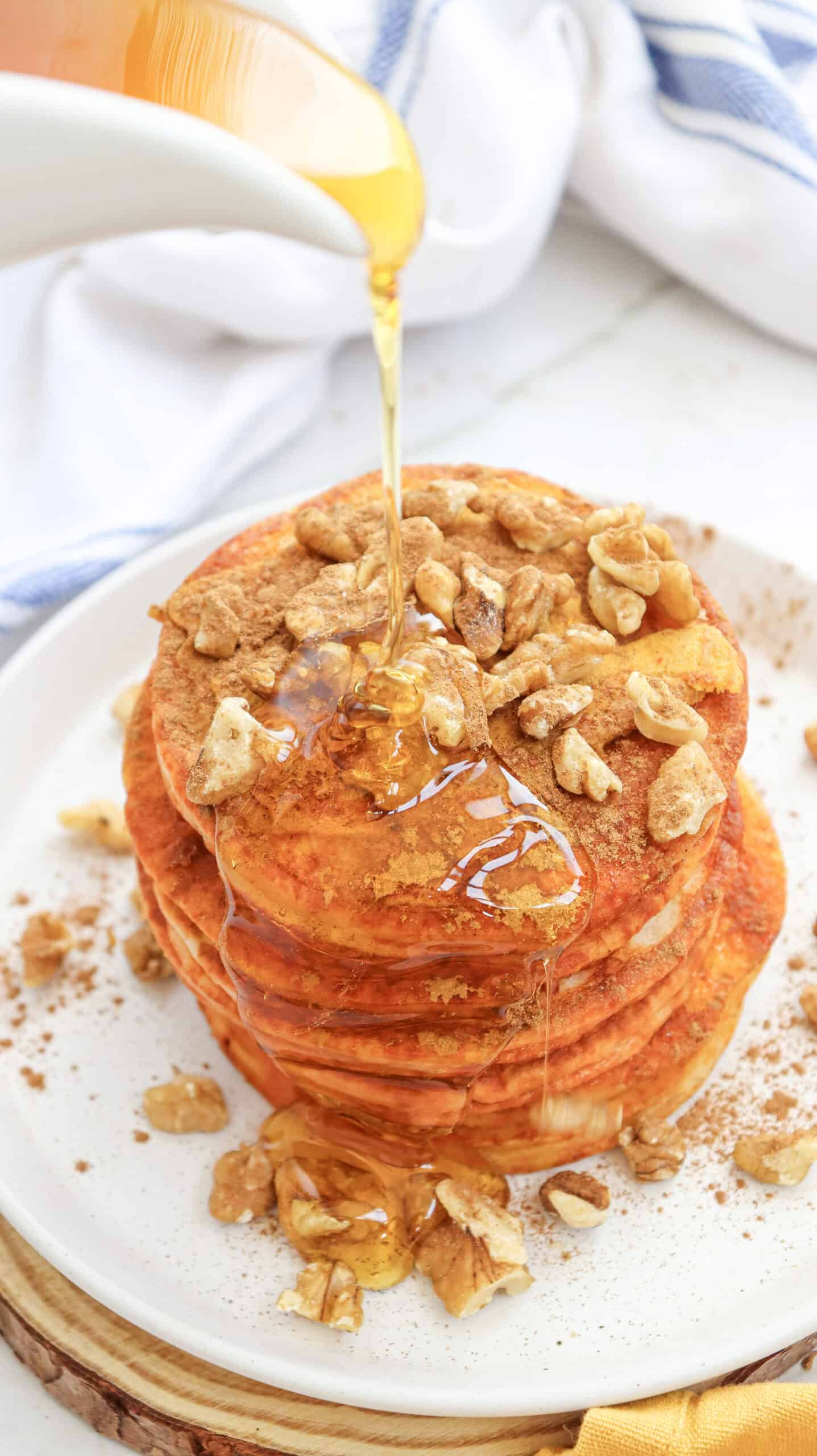 Close-up image of syrup being poured over a stack of pumpkin pancakes on a plate.