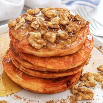 Close-up image of a stack of pumpkin pancakes with syrup and chopped walnuts on a plate.