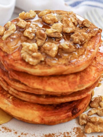 Close-up image of a stack of pumpkin pancakes with syrup and chopped walnuts on a plate.