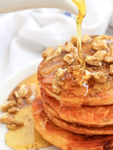 Close-up image of syrup being poured over a stack of pumpkin pancakes on a plate.