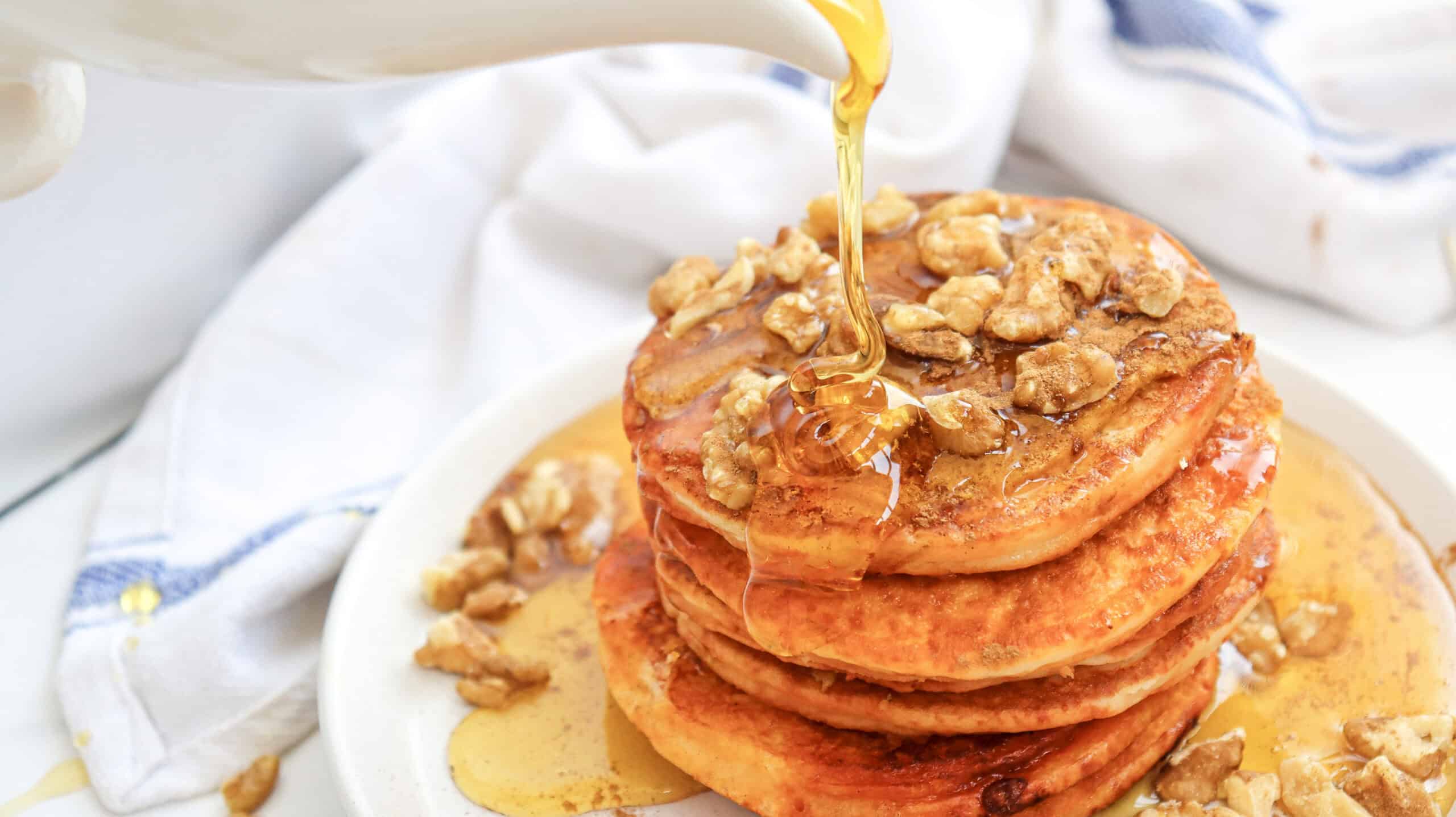 Close-up image of syrup being poured over a stack of pumpkin pancakes on a plate.