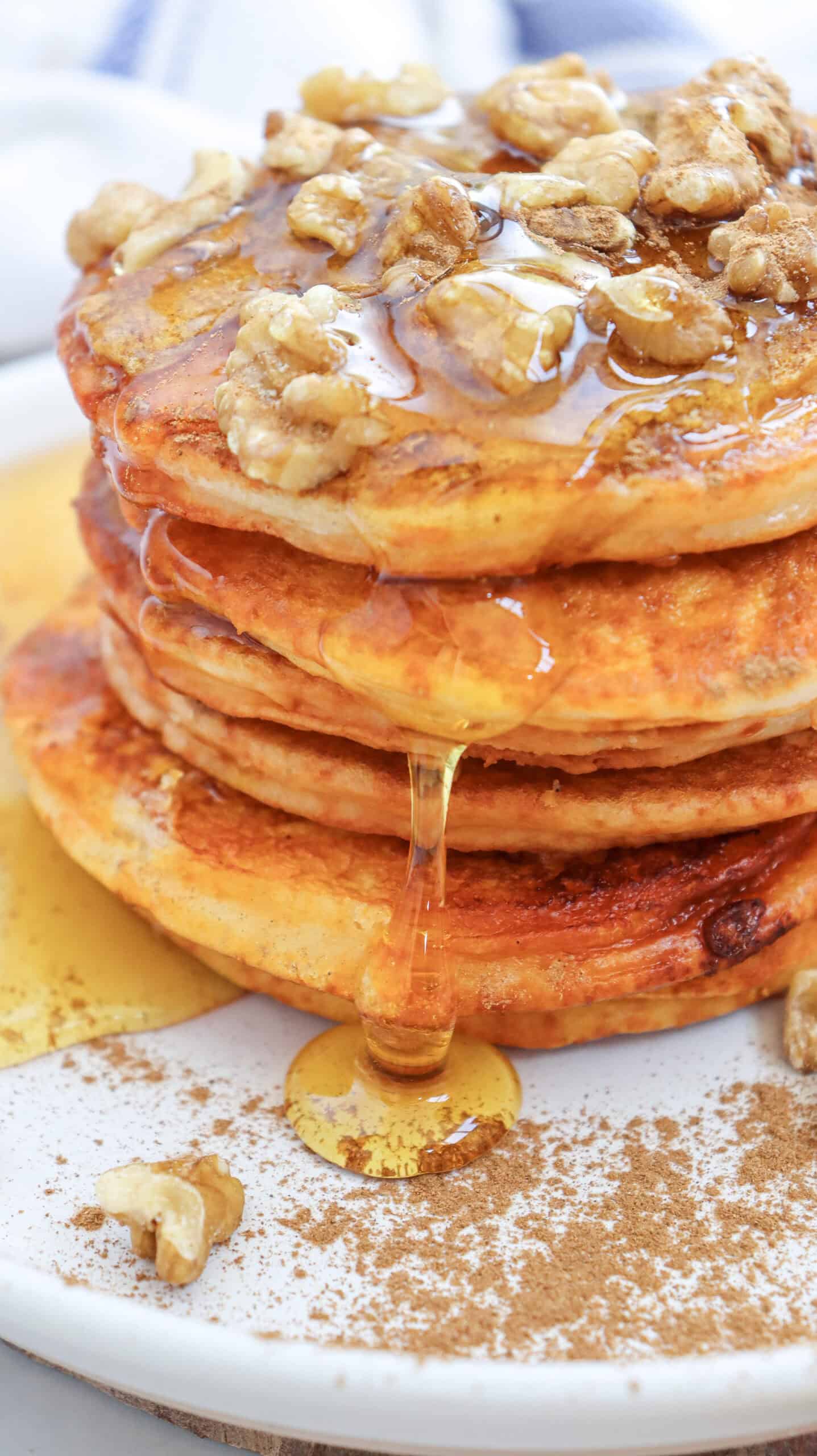 Close-up image of a stack of pumpkin pancakes with syrup and chopped walnuts on a plate