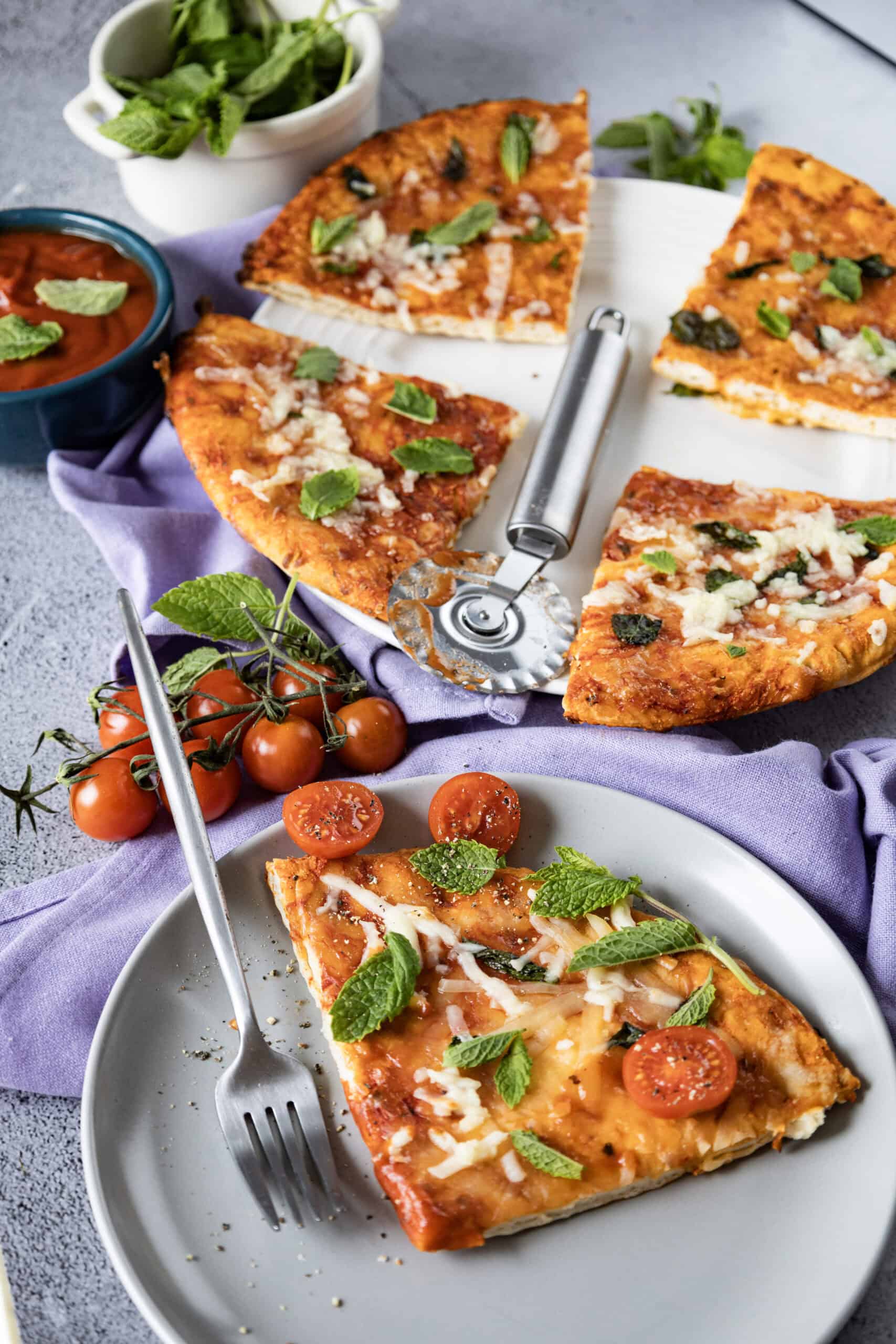 Close-up image of a slice of homemade Margherita pizza with a fork on a plate. Four additional slices and a pizza cutter are on a separate plate in the background.