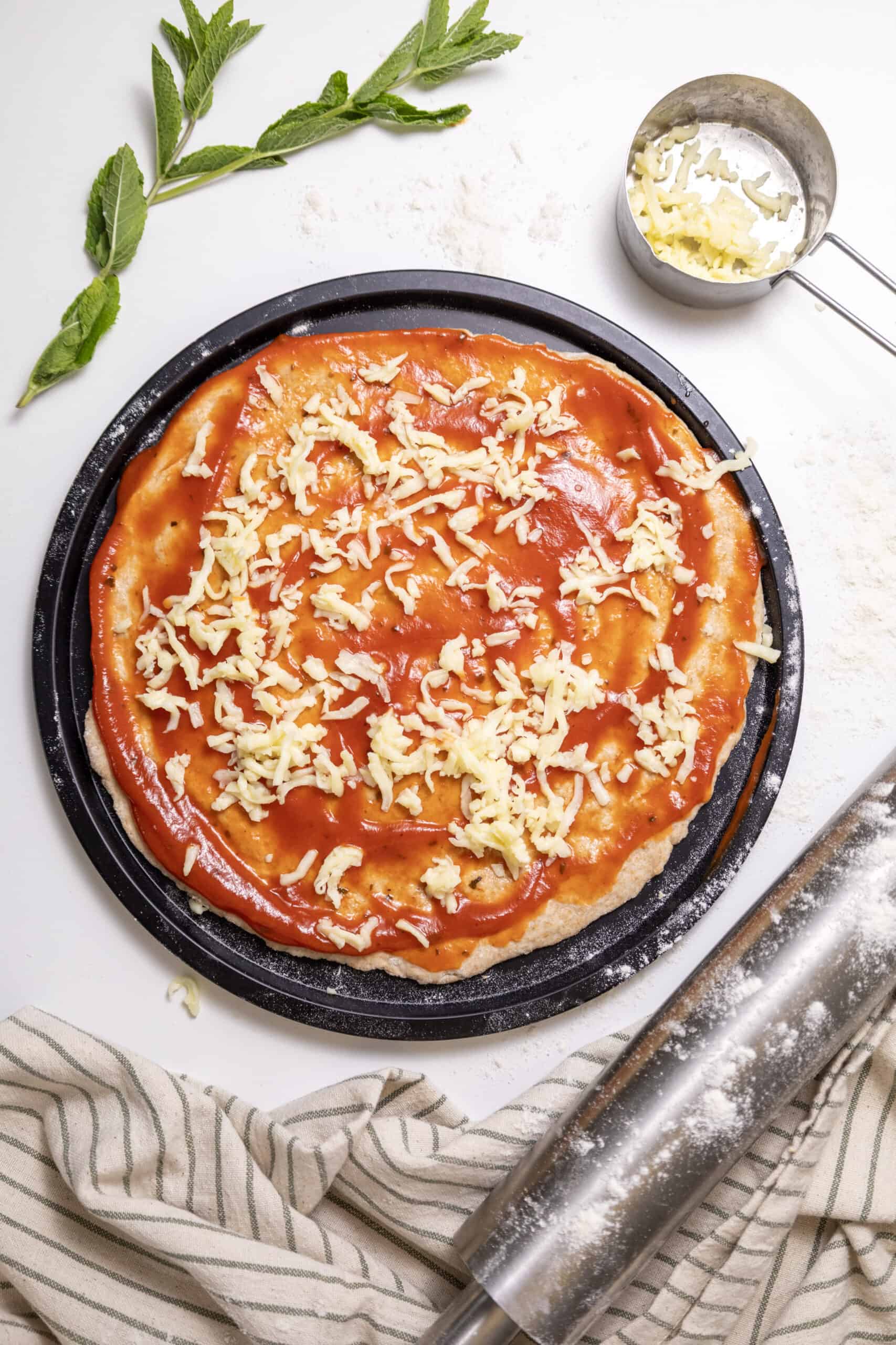 Pizza dough in a pizza pan with sauce and grated cheese spread on top.