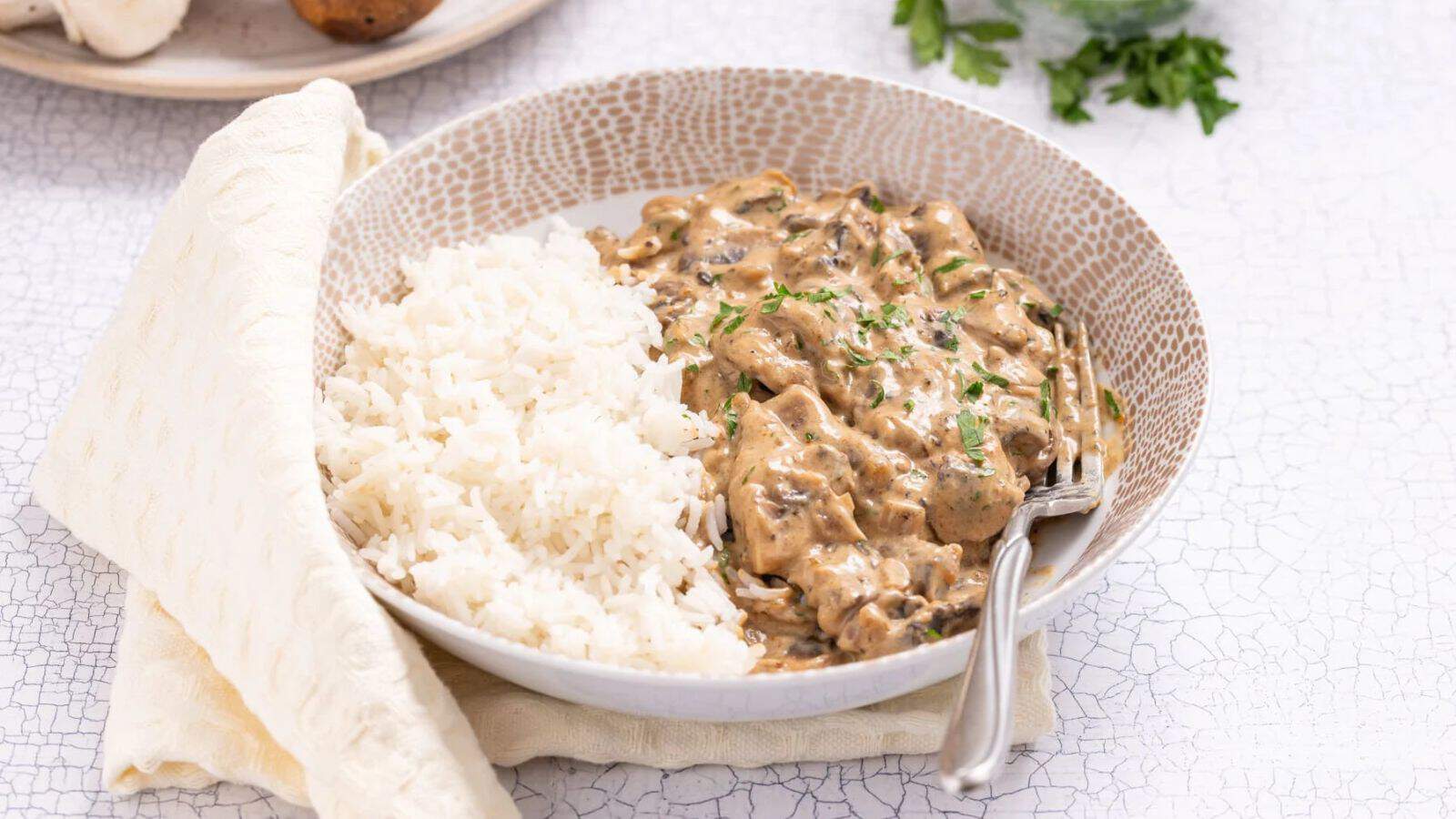 An image of mushroom stroganoff and white rice on a plate, with a fork on the side.