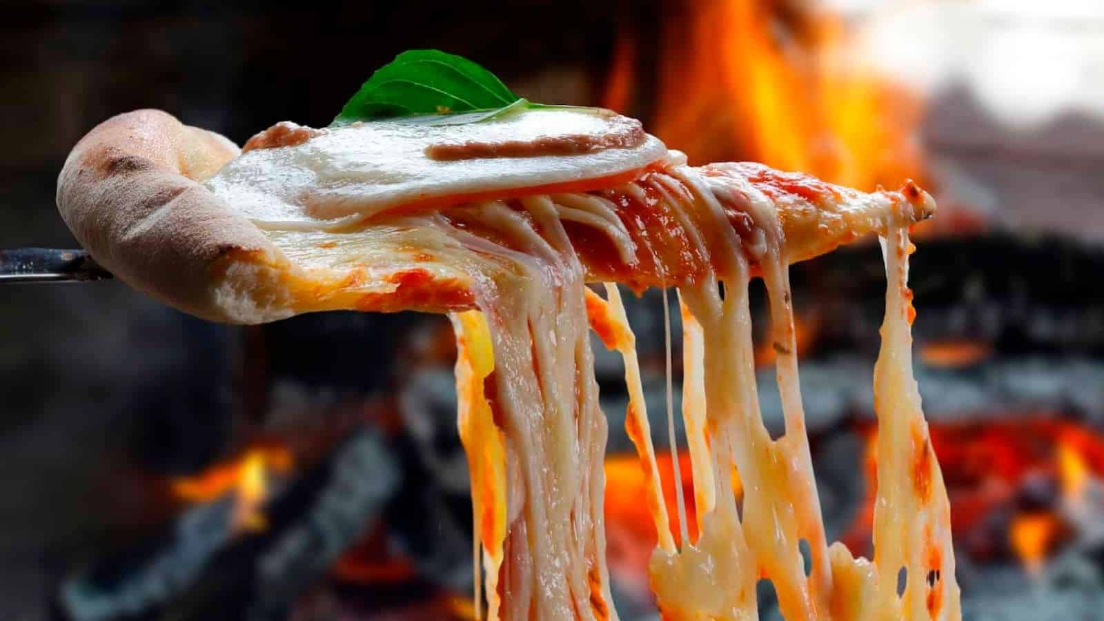 A slice of pizza is being held up by a fork in front of a fireplace.