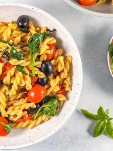 A plate of One Pot Pasta with Spinach and Tomatoes with a bowl of fresh spinach on the side.