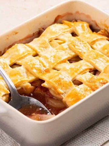 An image of peach cobbler in a baking dish with a portion of it missing.