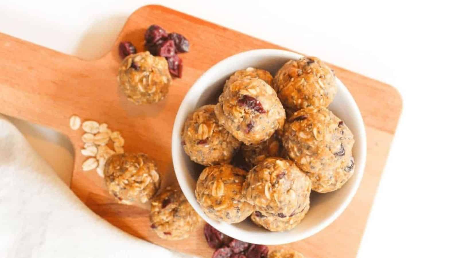 A stack of protein oat balls in a small white bowl sitting on a small wooden cutting board.