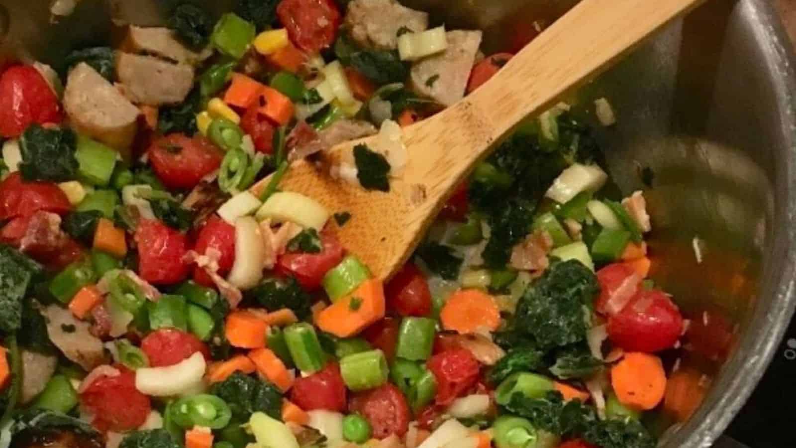 Sausage, kale and bean soup in pot with a wooden spoon.