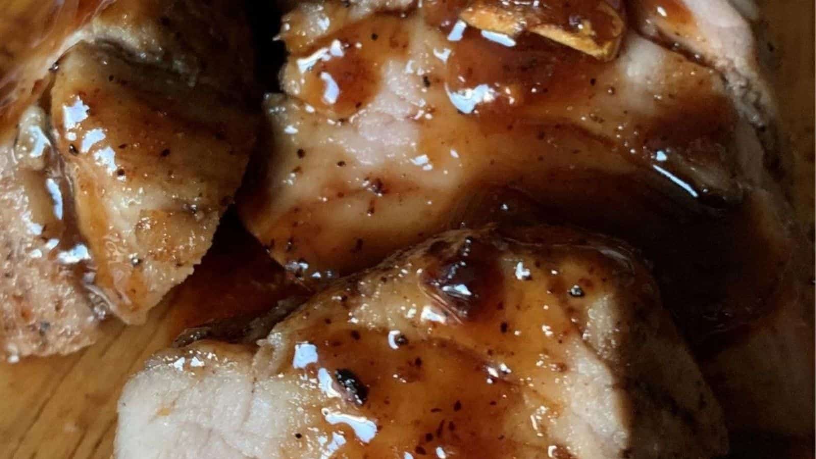 Slices of hot honey pork tenderloin on a cutting board with sauce.