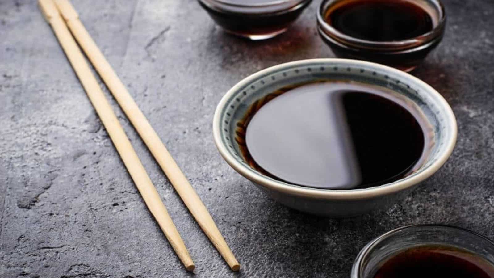 Small bowls of soy sauce with wooden chopsticks on dark background.