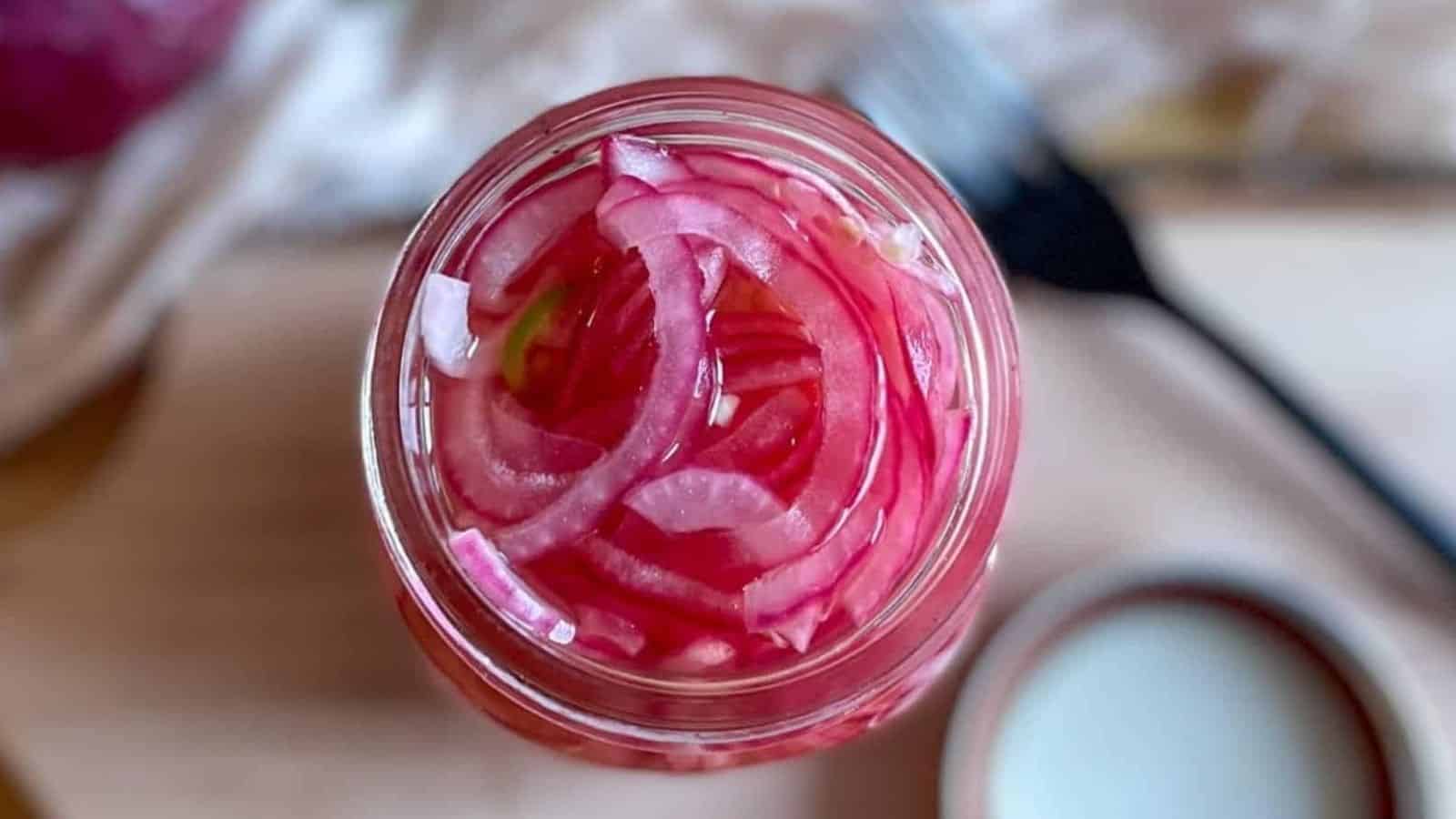 Overhead shot of spicy pickled onions in a glass jar.