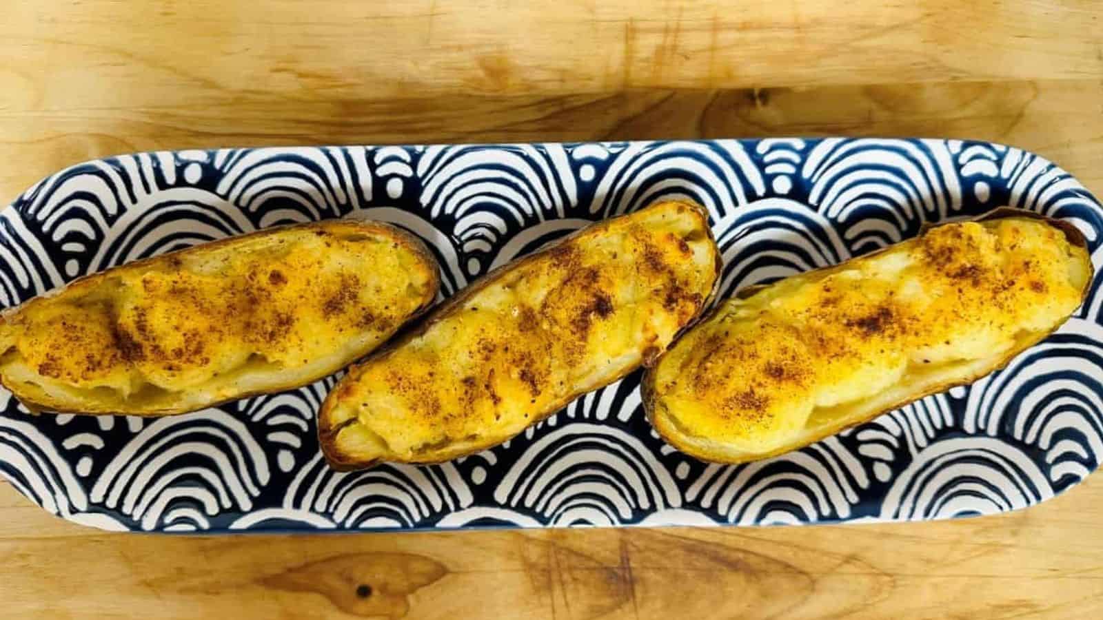 Three baked potatoes on a blue and white plate.