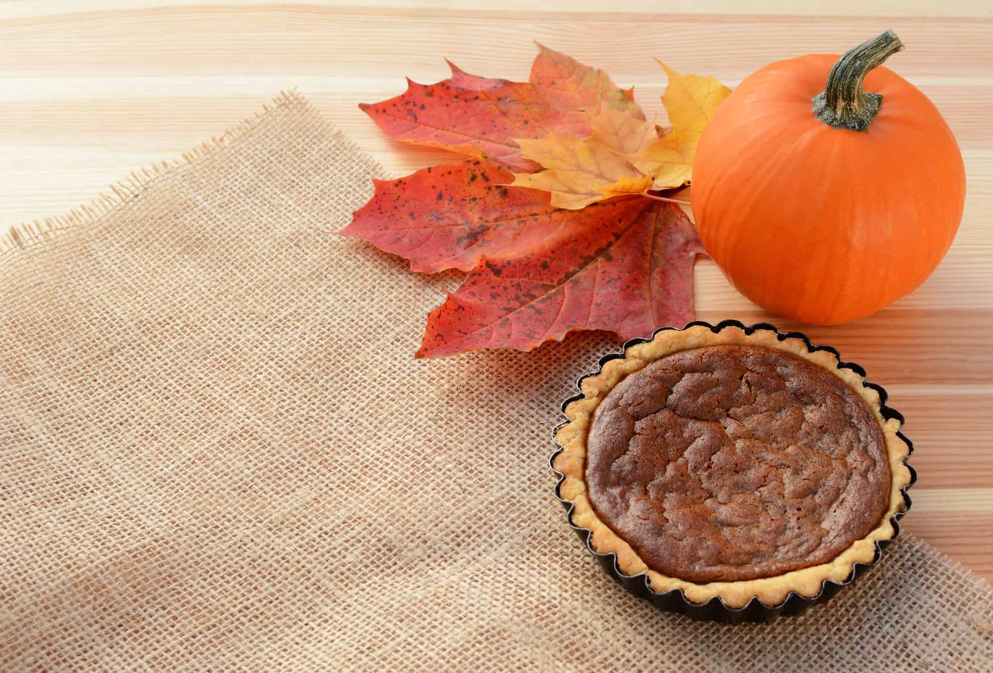 An image of a Sugar Pumpkin with a small pie and autumn leaves.