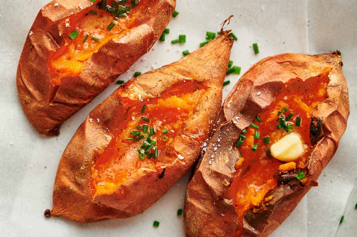 Three baked sweet potatoes with butter and chives on.