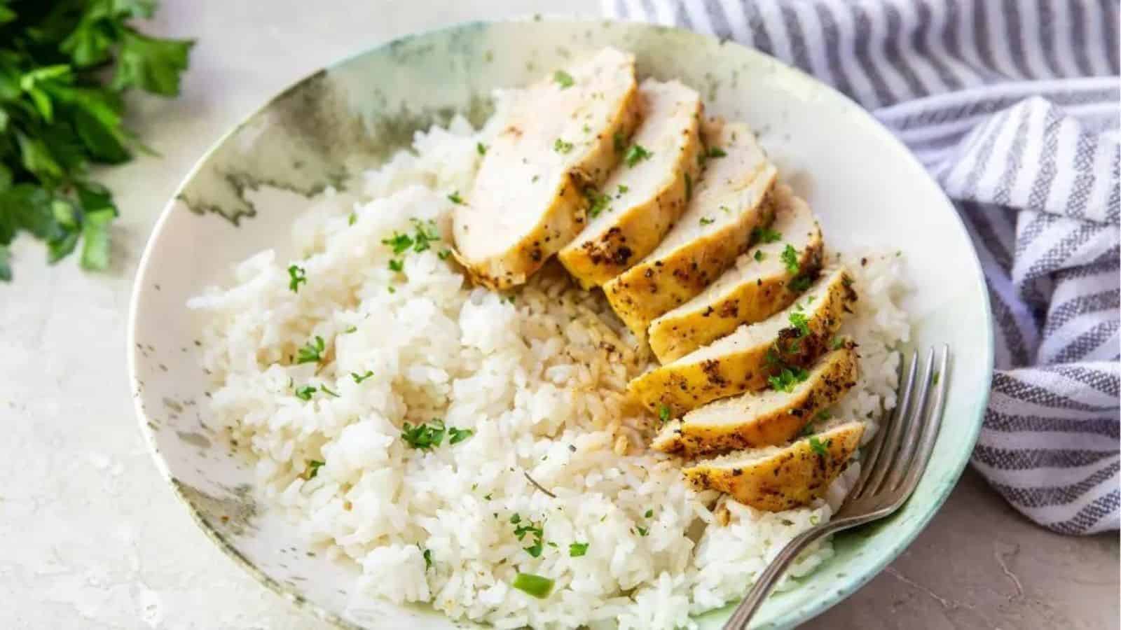 Air Fryer Lemon Pepper Chicken Breast on a white and teal plate with parsley, rice and a fork.