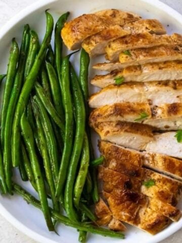 Blackstone Chicken Breast with green beans on a white plate with a fork.