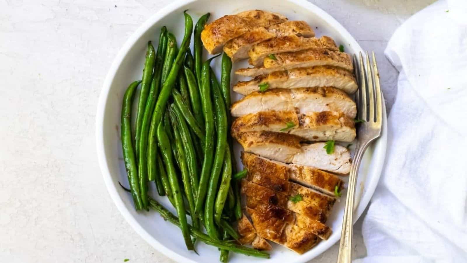 Blackstone Chicken Breast with green beans on a white plate with a fork.