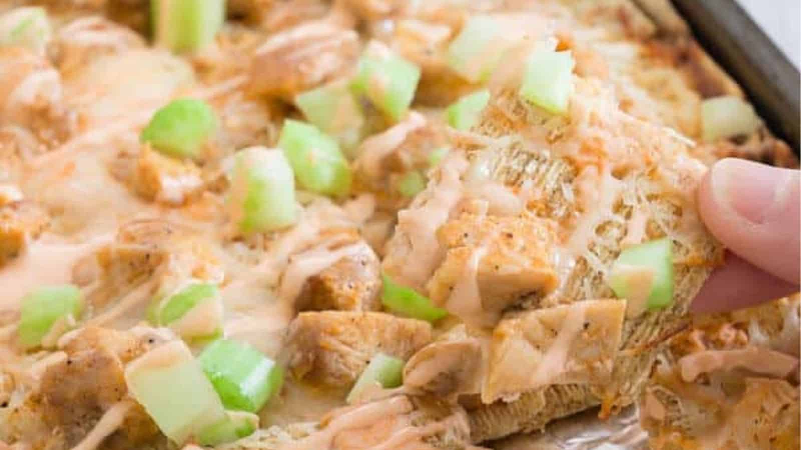 Close-up of a hand holding a piece of buffalo chicken trisuit nachos.