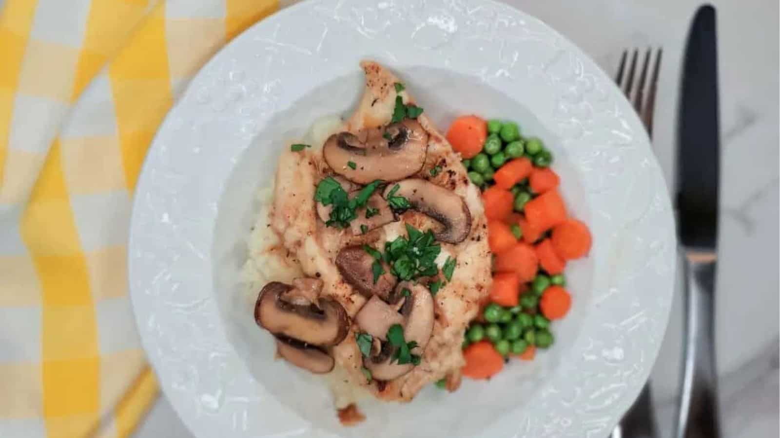 A bowl of chicken Marsala over mashed potatoes served with buttered peas and carrots.