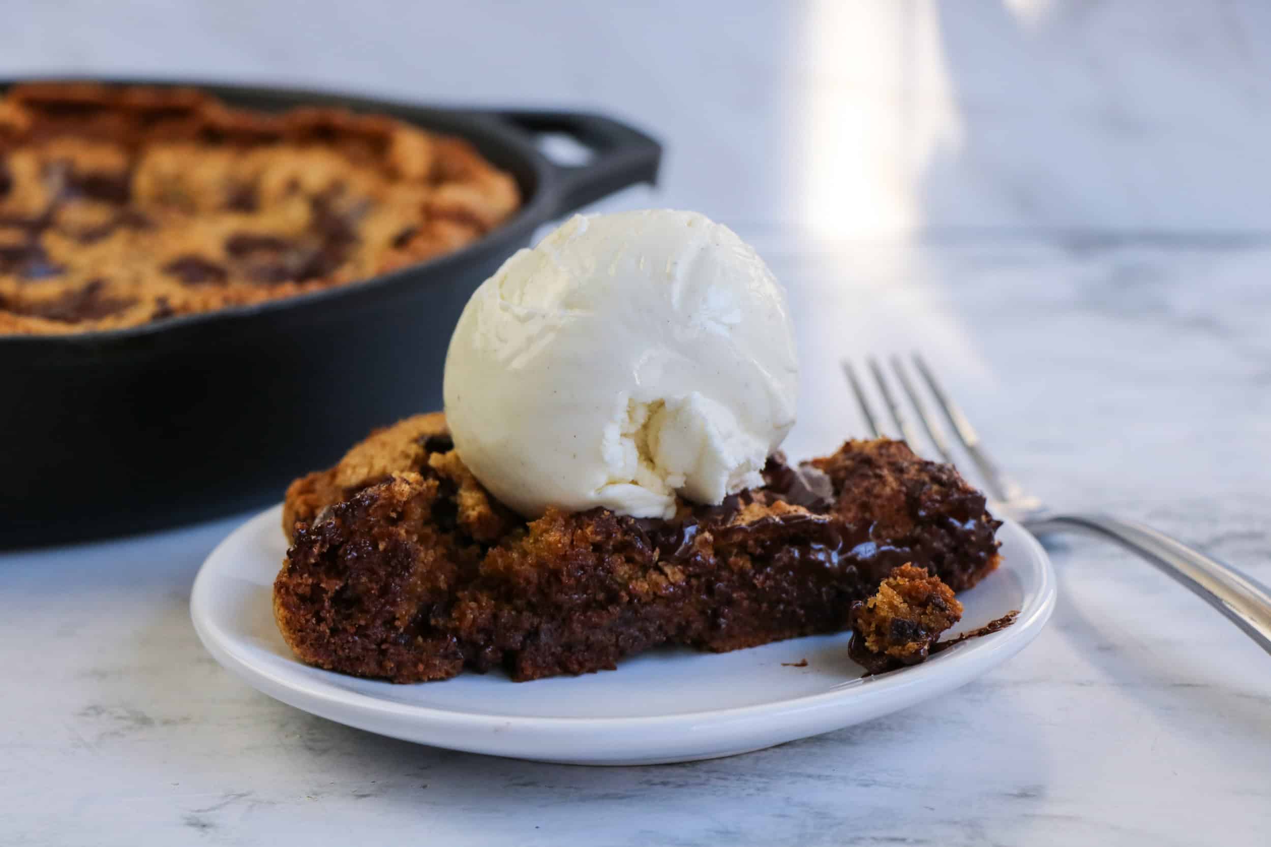 A slice of chocolate chip skillet cookie topped with a scoop of ice cream on a plate.