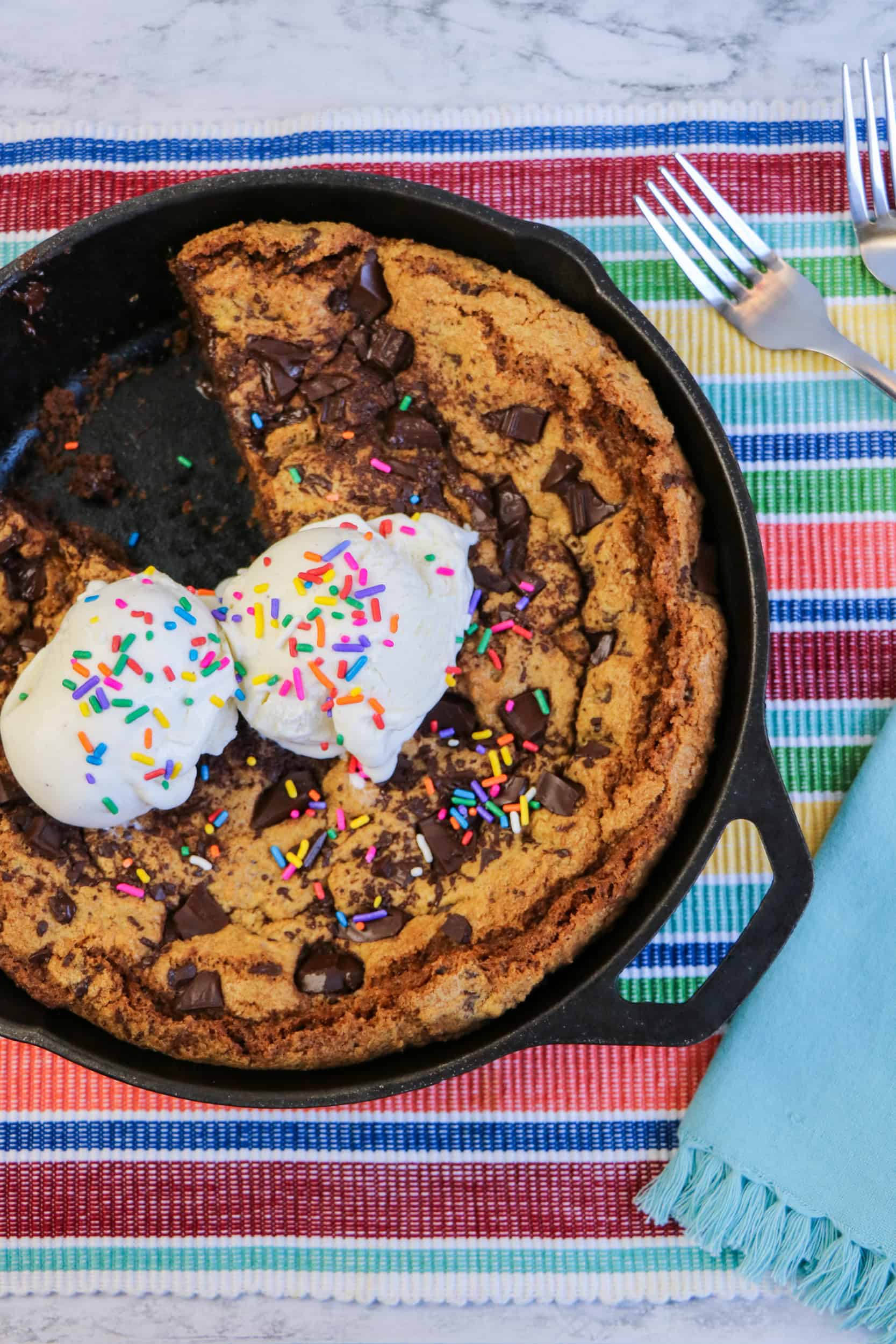 Top view of a chocolate chip skillet cookie topped with two scoops of ice cream and sprinkles, with one slice missing.