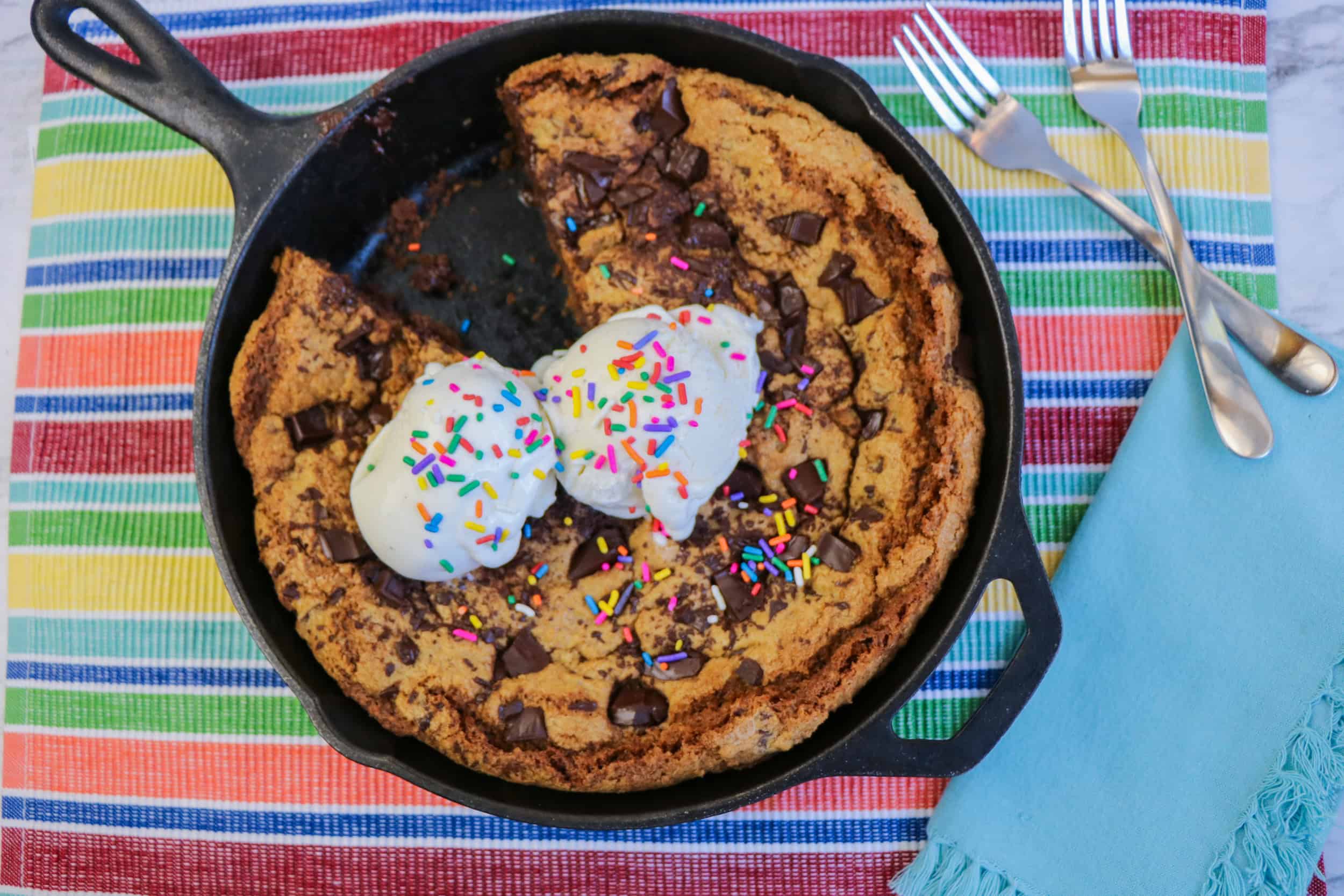 Top view of a chocolate chip skillet cookie topped with two scoops of ice cream and sprinkles, with one slice missing.