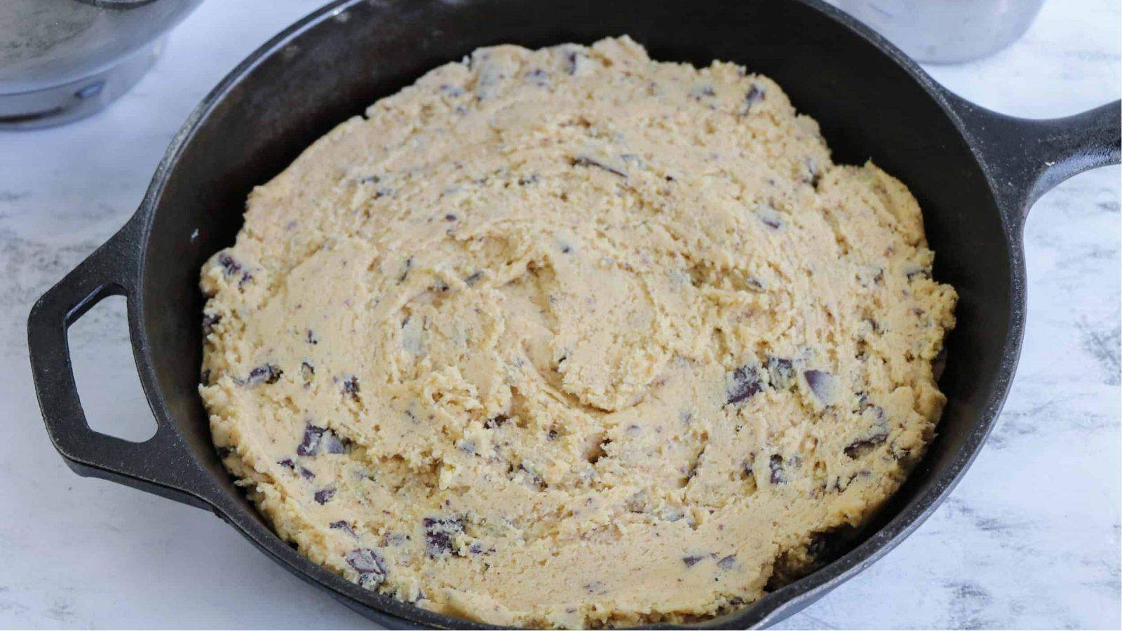 Chocolate chip skillet cookie batter spread evenly in a skillet.