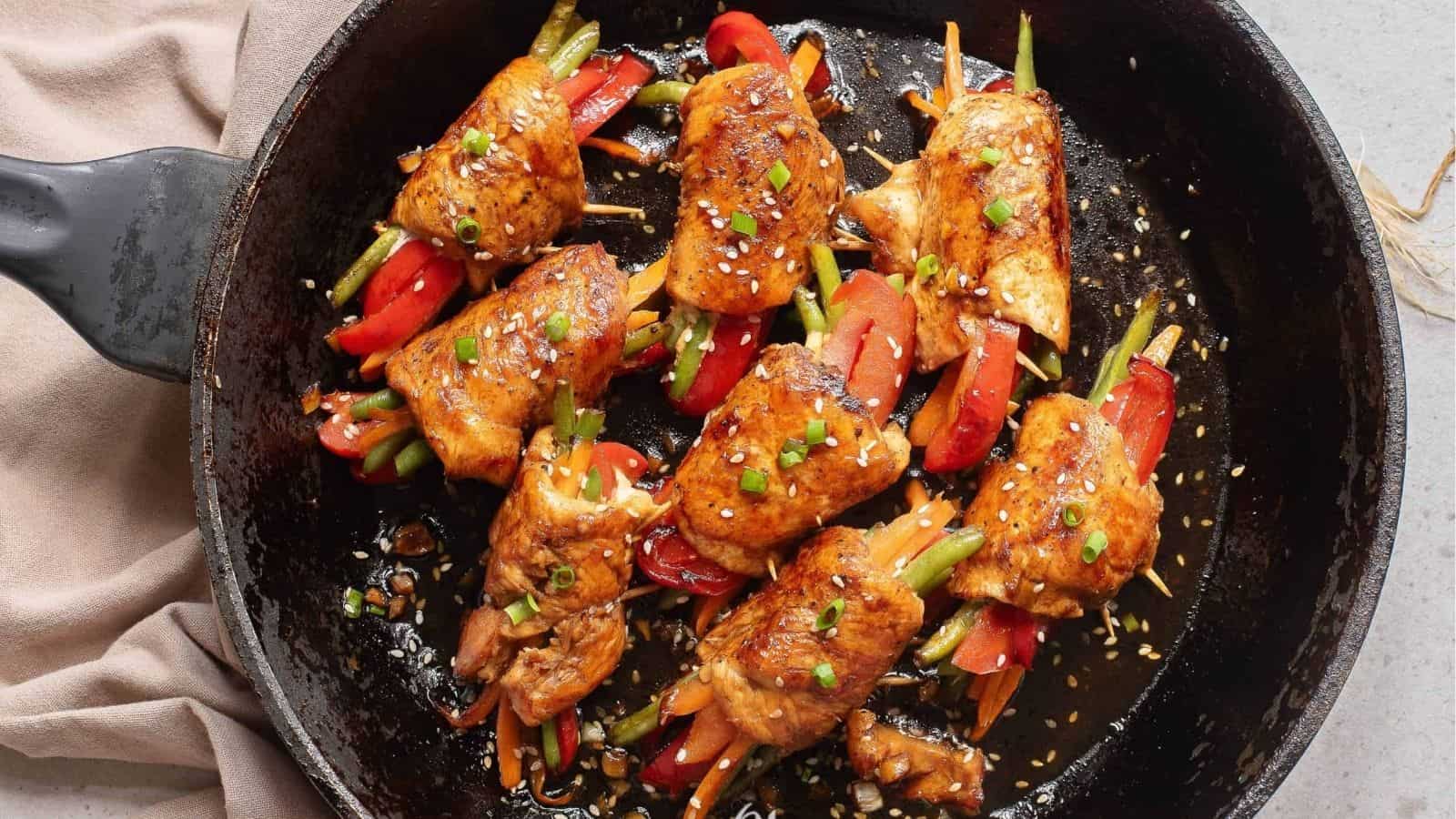 Vegetables wrapped in chicken cutlets in a skillet.