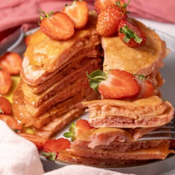 Close-up image of a stack of Strawberry Delight Pancakes topped with sliced strawberries.