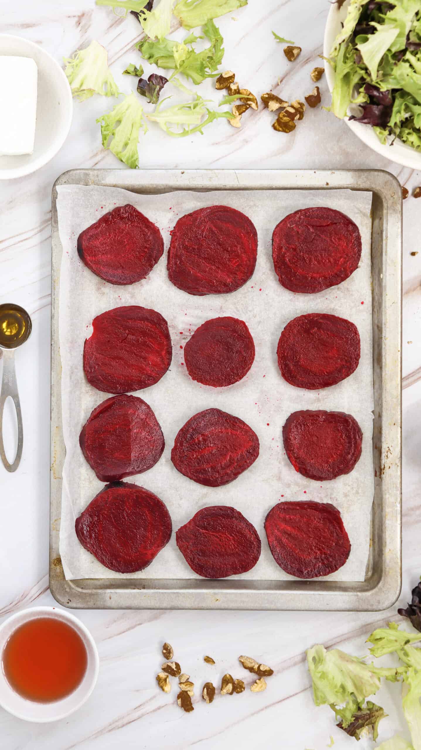 Overhead image of roasted beetroot slices neatly arranged on a baking sheet.