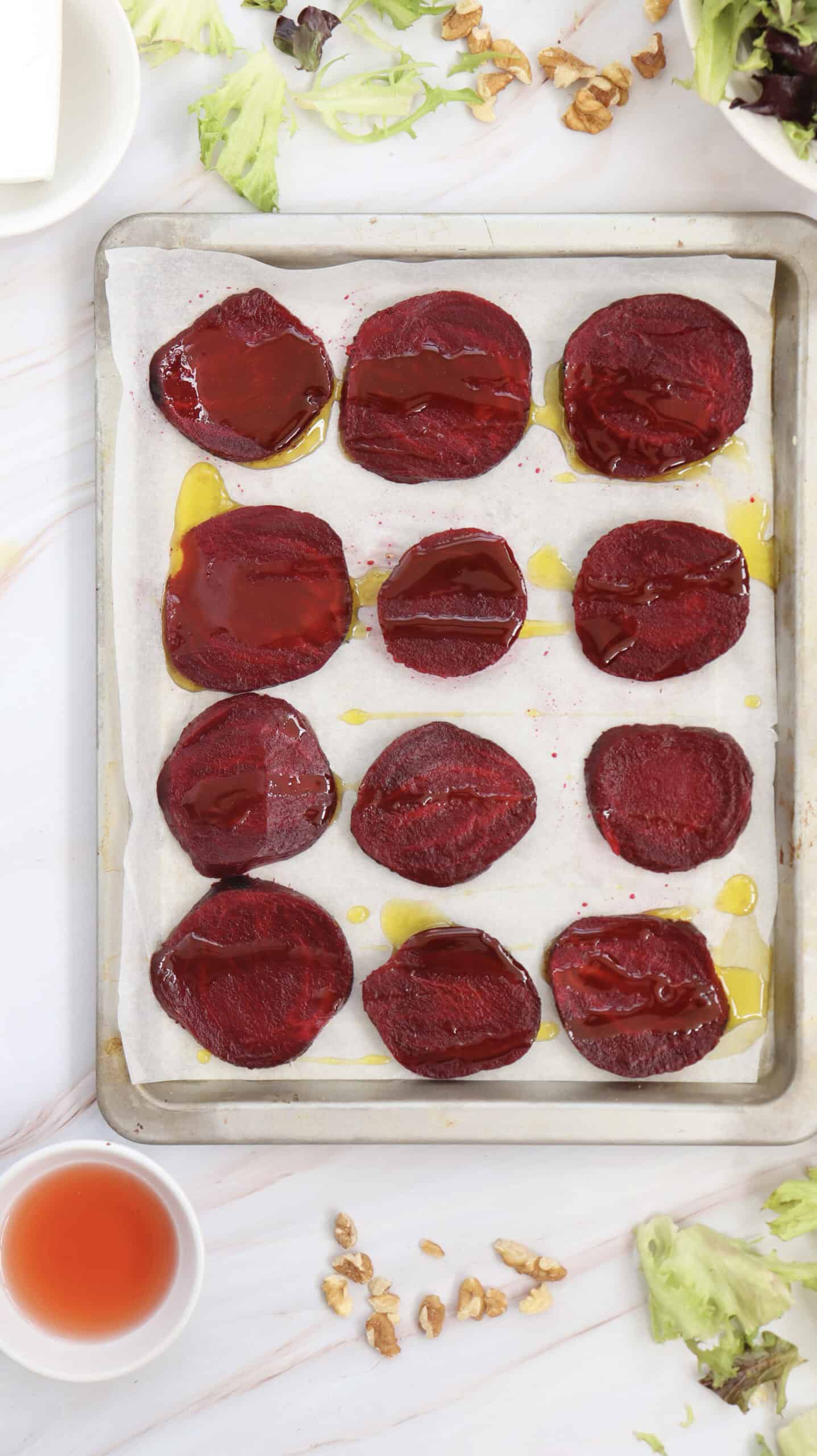 Overhead image of beetroot slices neatly arranged on a baking sheet.