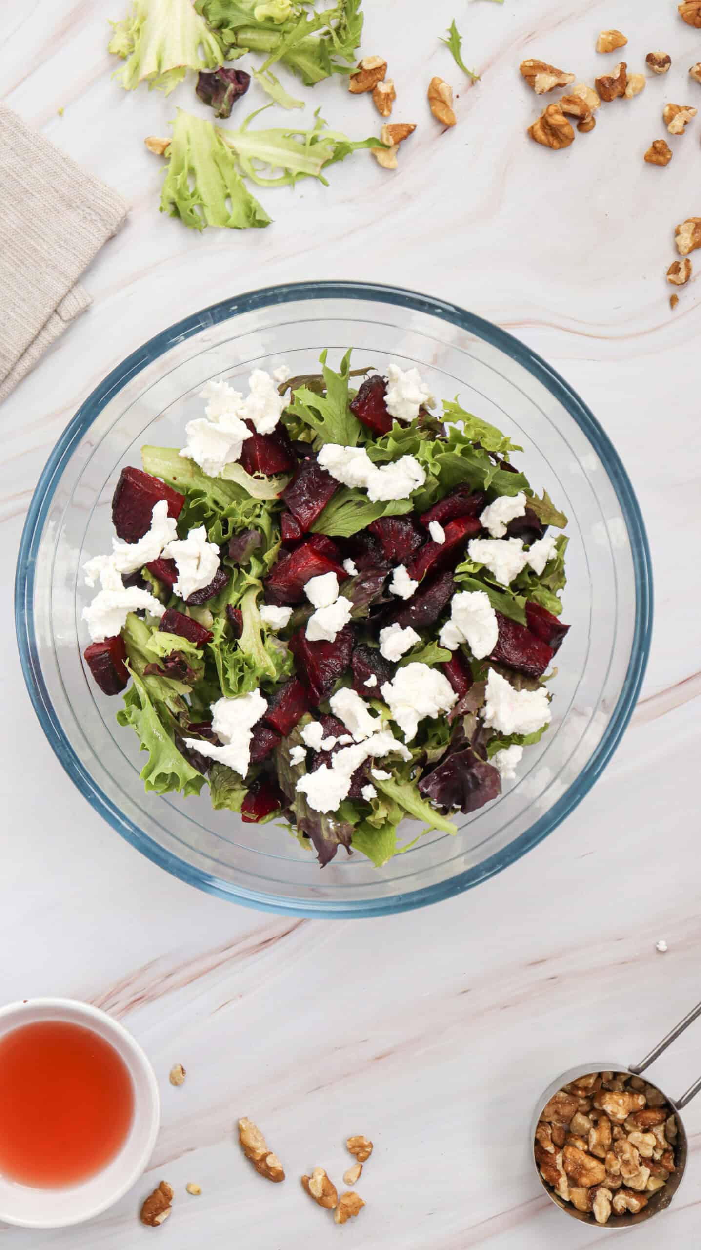 Overhead image of the salad mix in a glass bowl with chopped walnuts and red vinaigrette in the background.